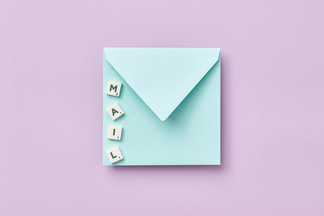 Minimalist flat lay showing a blue envelope and MAIL spelled with Scrabble tiles on a purple background.